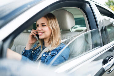 Eine junge Fahrerin mit Smartphone sitzt im Auto und telefoniert. - HPIF18557