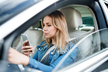 Eine junge Fahrerin sitzt im Auto und benutzt ihr Smartphone. - HPIF18558