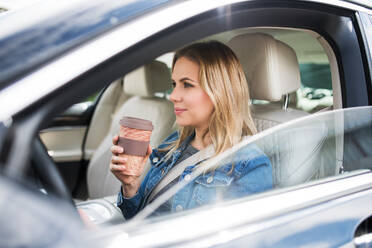 Eine junge Fahrerin sitzt im Auto und trinkt Kaffee aus einem Pappbecher. - HPIF18559