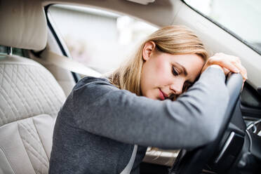 A tired young woman driver sitting in car, head resting on steering wheel. - HPIF18565