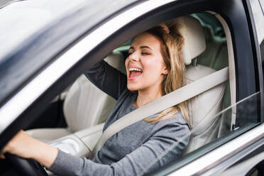 Eine fröhliche junge Fahrerin sitzt im Auto und fährt. - HPIF18567