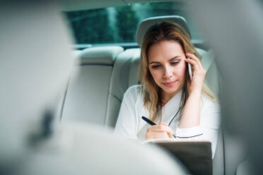 Geschäftsfrau mit Smartphone auf dem Rücksitz eines Taxis sitzend, telefonierend. - HPIF18575