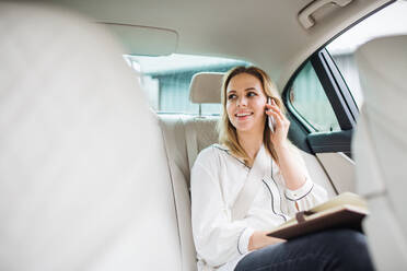 Geschäftsfrau mit Smartphone und Laptop auf dem Rücksitz eines Taxis sitzend, telefonierend. - HPIF18576