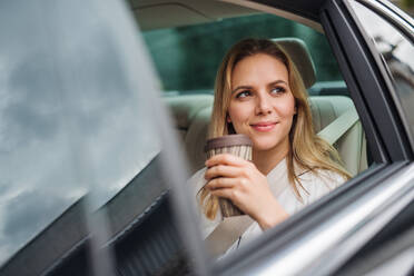 A business woman with coffee sitting on back seats in taxi car. - HPIF18578