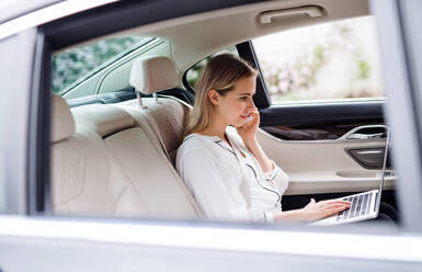 Geschäftsfrau mit Smartphone und Laptop auf dem Rücksitz eines Taxis sitzend, telefonierend. - HPIF18580