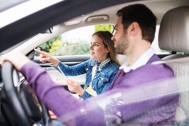 A happy young couple with smartphone sitting in car, talking. - HPIF18585