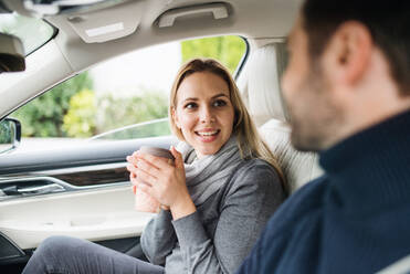 Ein glückliches junges Paar sitzt mit Kaffee im Auto und unterhält sich. - HPIF18588