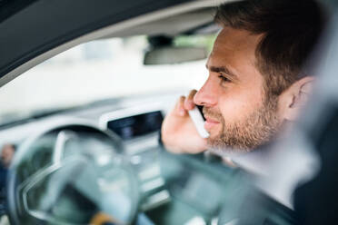 Close-up of young businessman with smartphone sitting in car, making phone call. - HPIF18591