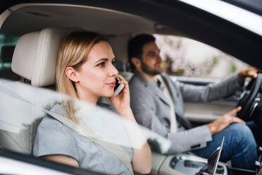 A happy young couple sitting in car, making a phone call. - HPIF18593