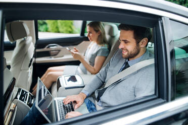 Junges Geschäftsehepaar mit Laptop, das auf dem Rücksitz im Auto sitzt und arbeitet. - HPIF18595