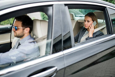 Geschäftsfrau mit Fahrer auf dem Rücksitz eines Taxis sitzend, telefonierend. - HPIF18597