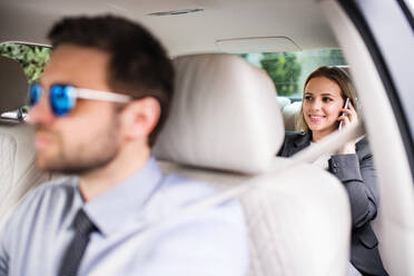 Geschäftsfrau mit Smartphone sitzt auf dem Rücksitz eines Taxis und telefoniert. - HPIF18598