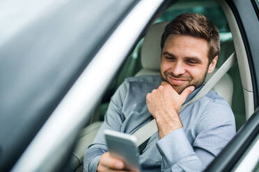 Junger Geschäftsmann mit Hemd, Krawatte und Smartphone sitzt im Auto und schreibt eine SMS. - HPIF18602