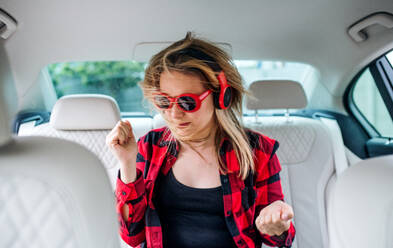 Ein Porträt einer jungen Frau mit Sonnenbrille und Telefon, die im Auto sitzt und sich amüsiert. - HPIF18612