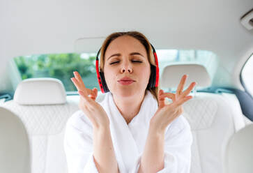 Junge Frau mit Kopfhörern im Auto sitzend, im Morgenmantel, entspannend. - HPIF18615