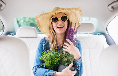 Eine junge Frau mit Hut und Sonnenbrille sitzt im Auto und hält Pflanzen. - HPIF18622