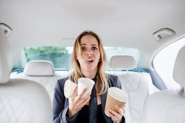 Young frustrated woman with empty paper glasses sitting in car, longing for coffee. - HPIF18624