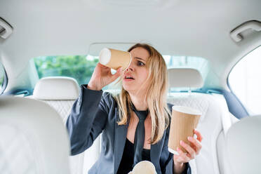Junge frustrierte Frau mit leeren Papiergläsern, die im Auto sitzt und sich nach einem Kaffee sehnt. - HPIF18626