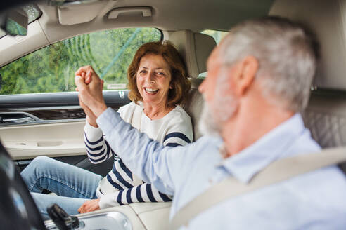 A happy senior couple with smartphone sitting in car, talking. - HPIF18635