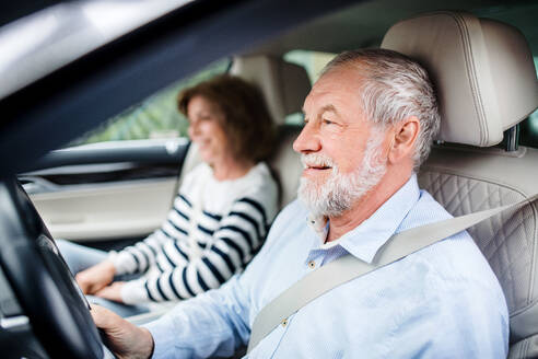 Ein glückliches älteres Ehepaar mit Smartphone sitzt im Auto und fährt. - HPIF18636