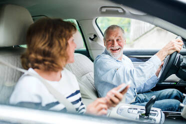 Ein glückliches älteres Paar mit Smartphone im Auto sitzend, das einen Ausflug macht. - HPIF18640
