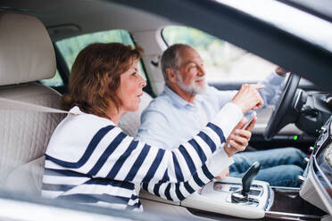 Ein glückliches älteres Paar mit Smartphone sitzt im Auto und unterhält sich. - HPIF18641
