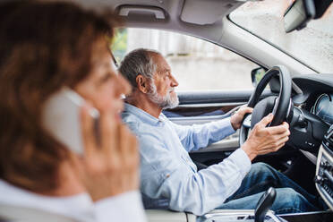 A happy senior couple with smartphone sitting in car, talking. - HPIF18642