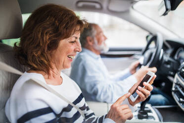 Ein glückliches älteres Paar mit Smartphone im Auto sitzend, das einen Ausflug macht. - HPIF18643