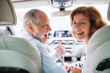 Rückansicht eines glücklichen älteren Paares, das im Auto sitzt und zurückblickt. - HPIF18644