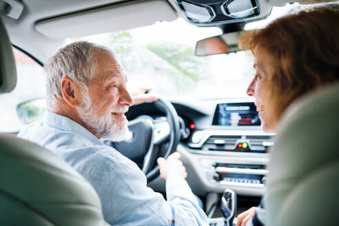 Eine Rückansicht eines glücklichen älteren Paares, das im Auto sitzt und sich unterhält. - HPIF18645