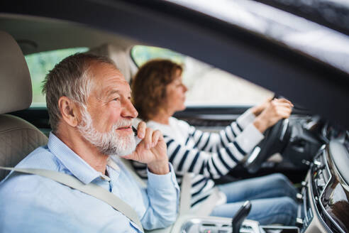 Ein glückliches älteres Paar mit Smartphone sitzt im Auto und unterhält sich. - HPIF18648