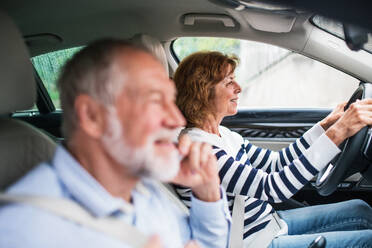 Ein glückliches älteres Paar mit Smartphone im Auto sitzend, das einen Ausflug macht. - HPIF18649