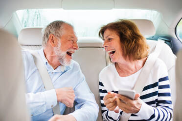 Ein fröhliches Seniorenpaar sitzt lachend auf der Rückbank eines Autos. - HPIF18651
