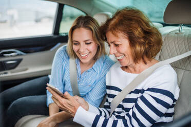 Zwei fröhliche Erwachsene sitzen auf den Rücksitzen im Auto und benutzen ein Smartphone. - HPIF18658