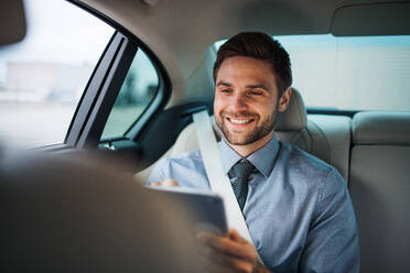 Ein Geschäftsmann mit Tablet sitzt auf dem Rücksitz eines Autos und arbeitet. - HPIF18668