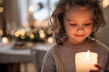 Porträt eines fröhlichen kleinen Mädchens zu Hause zu Weihnachten, das eine Kerze hält. - HPIF18687