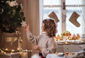 Seitenansicht eines glücklichen kleinen Mädchens, das zu Hause vor dem Weihnachtsbaum steht. - HPIF18690