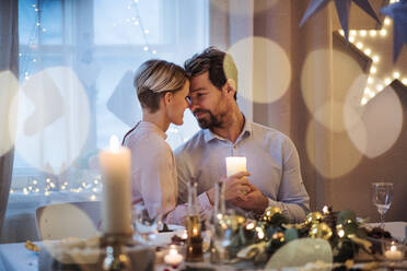 Frontansicht eines glücklichen Paares, das drinnen am Tisch Weihnachten feiert. - HPIF18702