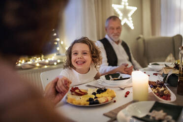 Glückliches kleines Mädchen mit Großeltern, die drinnen sitzen und gemeinsam Weihnachten feiern. - HPIF18706