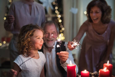 Small girl with parents and grandparents indoors celebrating Christmas, holding sparklers. - HPIF18737