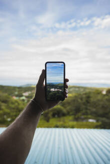 Hand eines Mannes, der ein Foto der Natur mit seinem Smartphone anklickt - RSGF00915