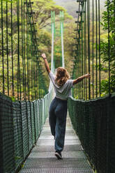 Carefree woman with arms outstretched walking on bridge - RSGF00922