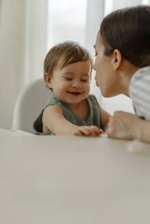 Mother blowing on face of smiling daughter at home - IEF00420