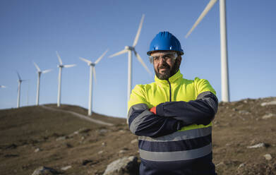 Älterer Ingenieur mit verschränkten Armen vor einer Windkraftanlage - SNF01666