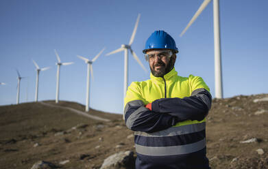 Mature engineer with arms crossed in front of wind turbines - SNF01666