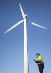 Engineer using tablet PC standing near wind turbine - SNF01670