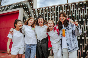 Happy teenage girls with arms around standing in front of wall at playground - MDOF01160