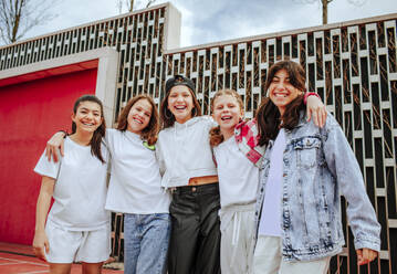 Smiling teenage girls with arms around standing in front of wall at playground - MDOF01161