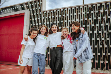 Fröhliche Mädchen im Teenageralter, die vor einer Mauer auf einem Spielplatz stehen - MDOF01162