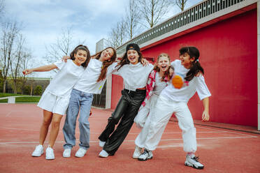 Playful teenage girls with arms around by wall at playground - MDOF01164